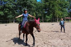 Uczestniczka wakacyjnej szkółki jeździeckiej  na koniu z instruktorką prowadzącą naukę  jazdy na lonży