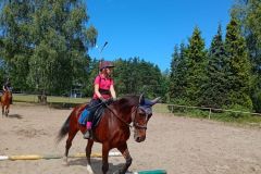 Uczestniczka wakacyjnej szkółki jeździeckiej pokonuje na koniu przeszkodę z leżących  drągów