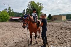 Uczestniczka wakacyjnej szkółki jeździeckiej na koniu z instruktorką  pomagającą dopasować strzemiona