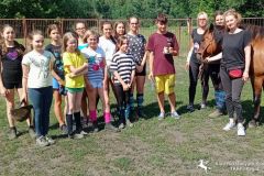 Kilkunastoosobowa grupa uczestników pierwszego turnusu wakacyjnej szkółki jeździeckiej  z instruktorkami i koniem