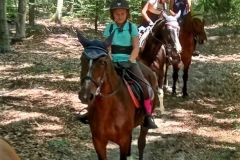 Trzyosobowa grupa uczestników wakacyjnej szkółki jeździeckiej  na koniach w trakcie wyjazdu w teren